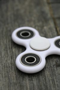 Ein weisser Fidget Spinner liegt auf einer dunklen Holzoberfläche. Fidget Spinner werden oft als Hilfsmittel eingesetzt, um die Konzentration bei ADHS Schweiz zu fördern. Bewegung und sensorische Reize helfen vielen Betroffenen in der Schweiz, ihre Aufmerksamkeit besser zu steuern.