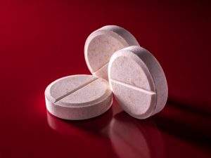 Drei runde, weiße Tabletten liegen nebeneinander auf einem intensiven roten Hintergrund. Die Bruchkerbe in der Mitte der Tabletten steht symbolisch für individuell anpassbare Dosierungen. Das Bild vermittelt eine klare, reduzierte Darstellung medikamentöser ADHS-Therapie.
