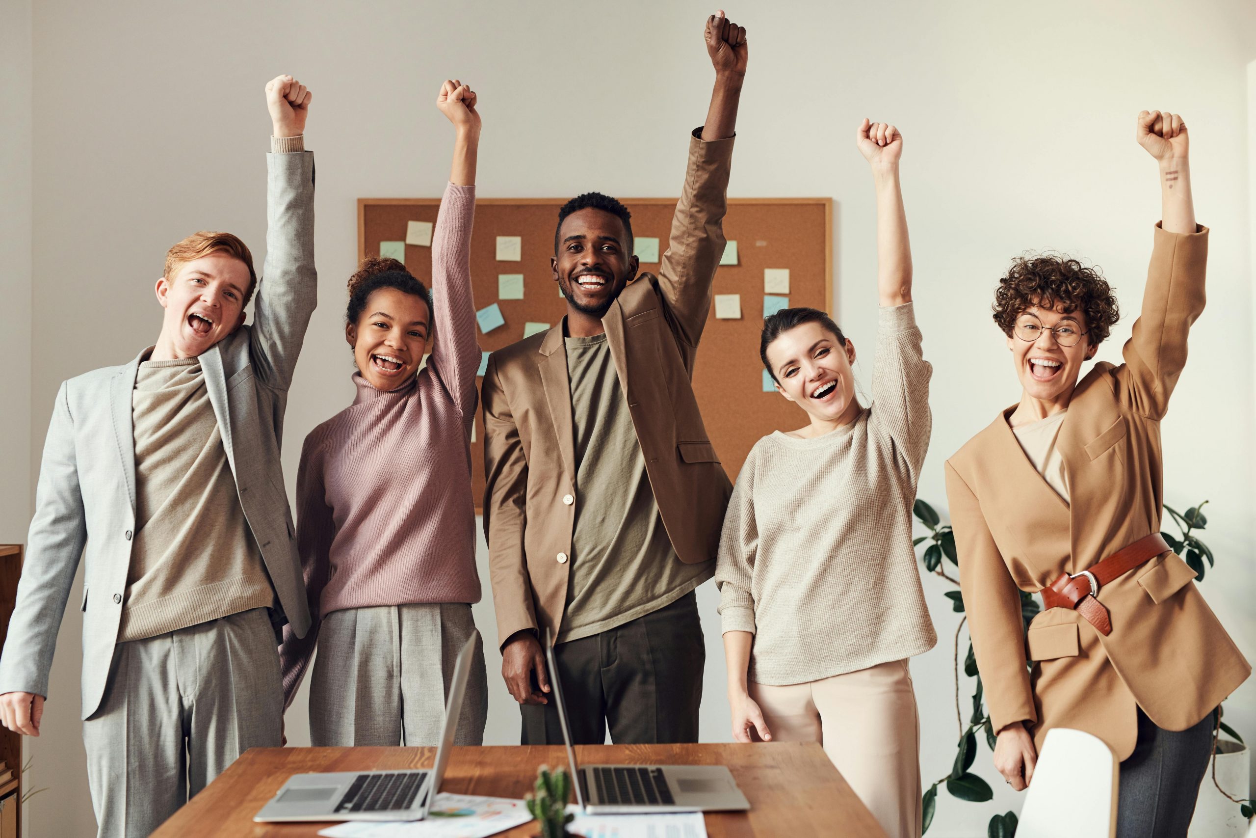 Fünf junge Erwachsene stehen freudestrahlend in einem modernen Büro und heben triumphierend die Arme. Das Bild vermittelt Teamgeist, Erfolg und ein positives Arbeitsumfeld – wichtige Faktoren bei der Berufswahl mit ADHS in der Schweiz.