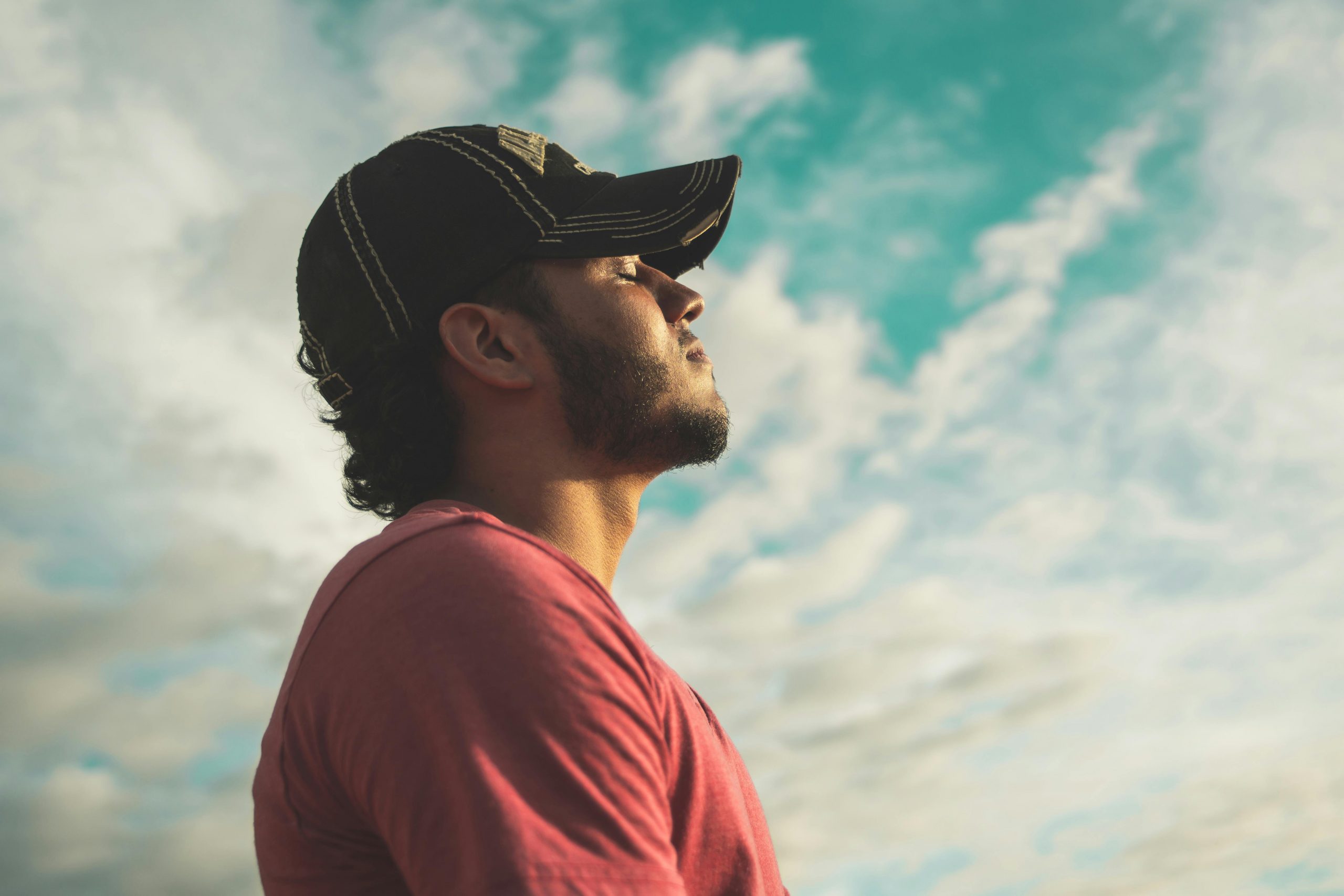 Ein Mann mit Kappe steht unter freiem Himmel, die Augen geschlossen, in einem Moment innerer Ruhe. Die Wolken am Himmel wirken beruhigend. ADHS Achtsamkeit Schweiz – bewusste Atempausen unterstützen die Selbstregulation.