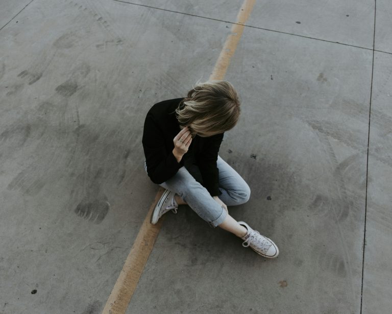 Eine junge Person sitzt allein auf dem Boden und hält sich nachdenklich den Kopf – ein Ausdruck von innerer Anspannung oder Erschöpfung. Dieses Bild symbolisiert die emotionale Überforderung, die viele Menschen mit ADHS in der Schweiz erleben, besonders in stressigen Alltagssituationen.