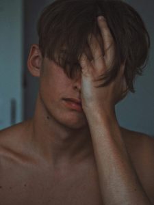 Ein junger Mann verdeckt sein Gesicht mit der Hand – Müdigkeit, Frustration oder innere Unruhe spiegeln sich in seiner Haltung. Bei ADHS kann sich Reizüberflutung in der Schweiz genau so zeigen: in Momenten, in denen die Gedanken nicht zur Ruhe kommen wollen.