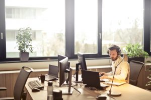 Ein konzentrierter Mitarbeiter arbeitet im modernen Büro mit mehreren Monitoren und Headset. Auch in der Schweiz gelingt es Menschen mit ADHS, im Beruf durch strukturierte Arbeitsumgebungen und Hilfsmittel fokussiert zu bleiben.