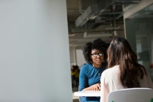 In einem vertraulichen Einzelgespräch in einem Büro tauschen sich zwei Frauen aus – möglicherweise ein Coaching oder Mentoring. Für Menschen mit ADHS in der Schweiz kann der berufliche Erfolg durch individuelle Unterstützung und Gespräche nachhaltig gefördert werden. Das Bild steht für zwischenmenschliche Verbindung und gezielte Förderung im Berufsleben.