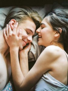 Ein junges Paar liegt entspannt im Bett und zeigt Zuneigung und Nähe. Solche Momente des Rückzugs und emotionaler Verbundenheit sind besonders wichtig, wenn ADHS im Beruf in der Schweiz eine Herausforderung darstellt.