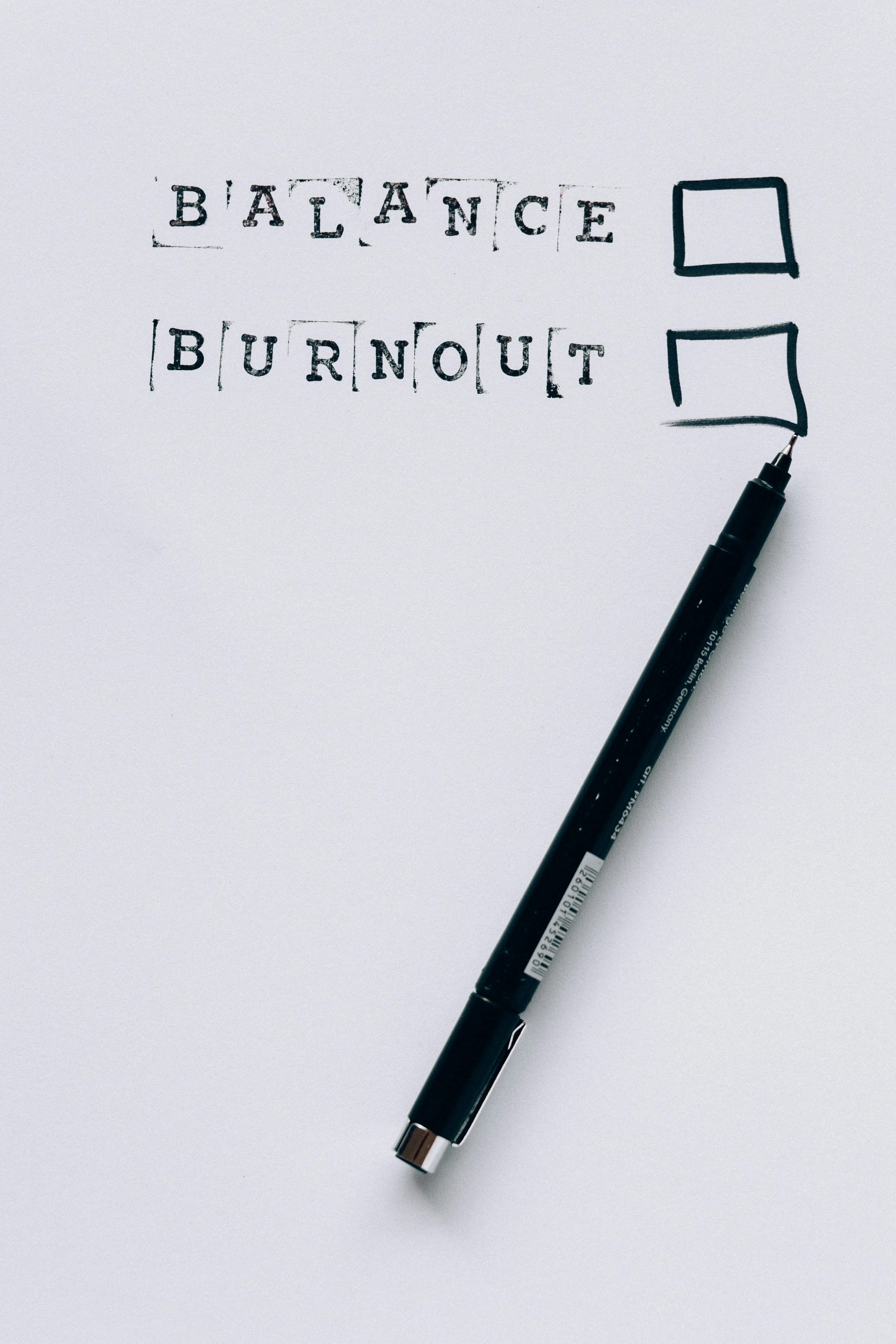 Ein Blatt Papier mit den Worten „Balance“ und „Burnout“, daneben Kästchen zum Ankreuzen und ein schwarzer Stift. Im Rahmen von ADHS Schweiz ist die Balance zwischen Belastung und Erholung ein zentrales Thema, um Burnout vorzubeugen. Die visuelle Darstellung regt zur Reflexion über den eigenen Zustand an.