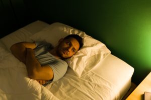 Ein junger Mann liegt abends wach im Bett und starrt nachdenklich an die Decke. Der Schlaf fällt ihm offensichtlich schwer. Schlafstörungen können bei ADHS Schweiz eine grosse Belastung darstellen.