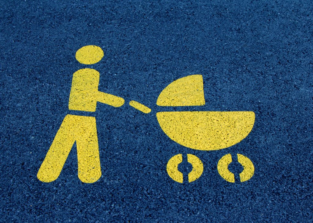 Eine gelbe Bodenmarkierung zeigt ein Elternsymbol mit Kinderwagen auf Asphalt. Dieses einfache Symbol steht für die täglichen Aufgaben von Eltern – in der Schweiz kann ADHS-bedingte Reizüberflutung dabei unbemerkt zu Überforderung führen.