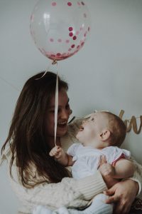 Eine Mutter hält ihr Baby auf dem Arm, beide lachen gemeinsam über einen Luftballon. Trotz der Freude kann die ständige Aufmerksamkeit, die Kinder fordern, bei ADHS schnell zur Reizüberflutung führen – auch in einem gut strukturierten Alltag in der Schweiz.