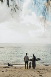 Ein Paar hält mit ihrem Kind an der Hand inne und blickt aufs Meer hinaus. Dieses Bild symbolisiert den Wunsch nach Balance zwischen familiären Bedürfnissen und beruflichen Herausforderungen, wie sie bei ADHS im Beruf in der Schweiz oft auftreten.