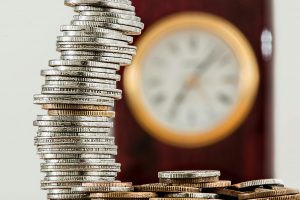 Ein schiefer Münzstapel vor einer verschwommenen Uhr symbolisiert instabile Finanzen und Zeitdruck. Für Menschen mit ADHS in der Schweiz verstärken solche Faktoren das Gefühl von Reizüberflutung und Kontrollverlust – besonders, wenn Budget und Zeitmanagement fehlen.