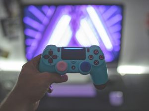 Ein stilvoller, türkisfarbener PlayStation-Controller wird vor einem lila beleuchteten Bildschirm gehalten – die Atmosphäre wirkt ästhetisch und immersiv. Gaming als fester Bestandteil der Freizeitgestaltung wird hier idealisiert. Auch bei ADHS Schweiz ist Gaming präsent – sowohl als Hobby als auch als potenzieller Auslöser für Überreizung.