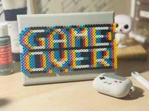 Ein kreatives Mosaikbild mit dem Schriftzug „GAME OVER“ aus Bügelperlen steht auf einem Schreibtisch, daneben liegt ein Gameboy-inspiriertes Case. Das Bild wirkt verspielt, aber auch symbolisch für digitale Überforderung. Gerade bei ADHS Schweiz ist der bewusste Umgang mit Bildschirmzeit und digitalen Reizen ein zentrales Thema.