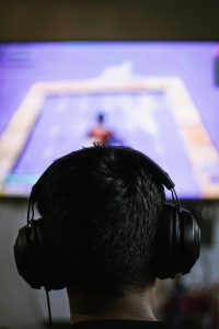 Eine Person mit Kopfhörern sitzt vor einem großen Bildschirm und spielt ein Videospiel – der Fokus liegt auf dem intensiven Eintauchen in die virtuelle Welt. Die Szene verdeutlicht die starke Anziehungskraft von Games. In der Diskussion um ADHS Schweiz spielt exzessives Gaming eine wichtige Rolle – sowohl als Symptom als auch als Bewältigungsstrategie.