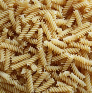 Eine grosse Menge ungekochter Fusilli-Nudeln liegt dicht aneinandergereiht. Die gedrehten Pasta-Formen wirken in ihrer Helligkeit und Struktur sehr lebendig. Bei ADHS Schweiz wird zunehmend erforscht, welchen Einfluss kohlenhydratreiche Ernährung auf die Konzentrationsfähigkeit hat.