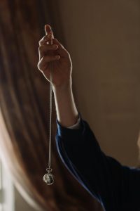 Eine Hand hält ein Hypnosependel vor einem weichen Hintergrund. Diese Szene symbolisiert die konzentrierte Arbeit in der ADHS Hypnose Schweiz, bei der innere Ruhe und Fokus im Vordergrund stehen.