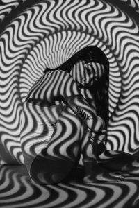 Eine Frau sitzt mit geschlossenen Augen in einem hypnotisch wirkenden Lichtmuster. Die spiralförmige Projektion erzeugt eine visuelle Tiefenwirkung – ideal zur Veranschaulichung von Trancezuständen in der ADHS Hypnose Schweiz.