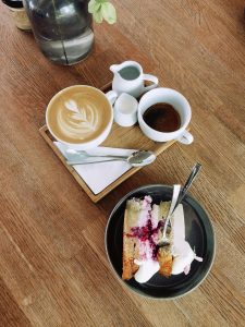 Auf einem Holztisch stehen Cappuccino, Espresso und ein Stück Kuchen mit Beeren und Sahne. Ein bewusster Umgang mit Zucker und Koffein ist für Menschen mit ADHS Schweiz wichtig, um Schwankungen im Energielevel zu vermeiden.