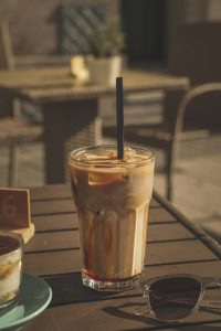 Ein Glas Eiskaffee mit Strohhalm steht auf einem Holztisch in der Sonne, daneben eine Sonnenbrille. Gerade bei ADHS Schweiz spielt der bewusste Konsum von koffeinhaltigen Getränken eine wichtige Rolle für den Tagesrhythmus.