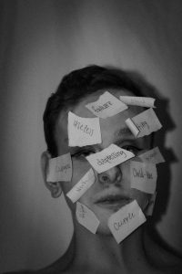 Schwarz-weiss Porträt eines Jugendlichen mit zahlreichen beschrifteten Zetteln im Gesicht – Wörter wie „failure“, „useless“ oder „depressing“ symbolisieren das Stigma, die Selbstzweifel und komorbiden Symptome wie Depression bei ADHS.