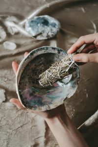 Eine Hand hält ein traditionelles Räucherbündel über einer Muschelschale – ein häufig genutztes Ritual in der Naturheilkunde. Solche Anwendungen können im Rahmen der Naturheilkunde bei ADHS in der Schweiz zur Förderung von Achtsamkeit und Entspannung eingesetzt werden.