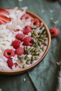 Eine bunte Smoothie Bowl mit frischen Himbeeren, knackigen Kürbiskernen und Kokoschips, liebevoll angerichtet. Diese nährstoffreiche Mahlzeit kann bei ADHS Schweiz eine ausgewogene Ernährung unterstützen und Konzentration fördern.
