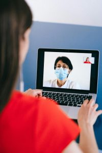 Eine Frau führt ein Videogespräch mit einer Ärztin, die eine Schutzmaske trägt und freundlich in die Kamera blickt. Die Szene zeigt eine sichere, diskrete Atmosphäre für sensible Gespräche. Online-Konsultationen ermöglichen eine flexible und ortsunabhängige Unterstützung – besonders hilfreich bei ADHS Schweiz, wo schnelle Hilfe gefragt ist.