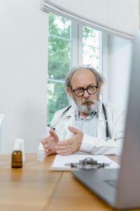 Ein erfahrener Arzt mit Brille und Stethoskop spricht während eines Videoanrufs ernsthaft in die Kamera. Auf dem Tisch vor ihm liegen medizinische Unterlagen und Medikamente – ein Hinweis auf eine strukturierte Beratungssituation. Solche digitalen Sprechstunden sind ein zentraler Bestandteil moderner Versorgungskonzepte bei ADHS in der Schweiz.