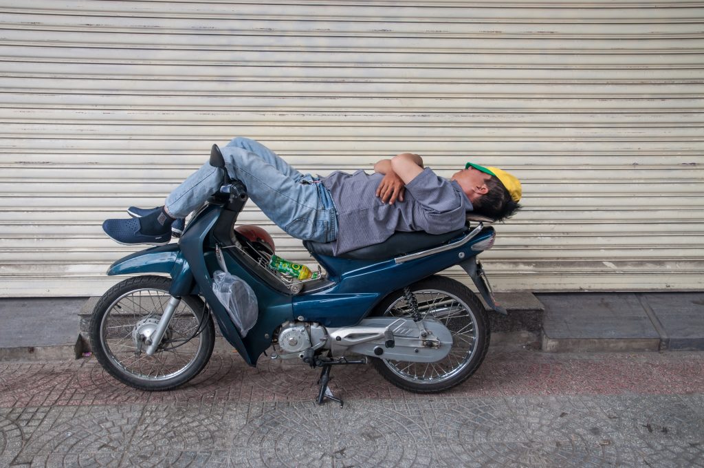 Ein Mann liegt entspannt auf einem Motorrad und macht ein Nickerchen auf der Strasse. Gerade bei ADHS Schweiz kann ausreichender Schlaf helfen, die Tagesmüdigkeit und Impulsivität besser zu kontrollieren. Ungewöhnliche Schlaforte zeigen, wie gross das Bedürfnis nach Erholung sein kann.