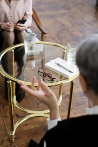 Eine Person spricht gestikulierend, während die andere aufmerksam zuhört. Auf dem Tisch liegt ein Notizbuch mit Brille – typische Symbole für therapeutische Sitzungen. Dieses Bild zeigt eine ADHS Therapie in der Schweiz in einem vertrauensvollen Rahmen.