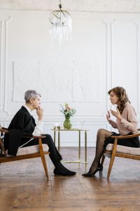 Zwei Frauen führen ein intensives Gespräch in einem hell eingerichteten Raum mit Blumen und Wasser. Die Szene wirkt professionell und gleichzeitig einladend. Sie steht beispielhaft für eine persönliche und stilvolle ADHS Therapie in der Schweiz.