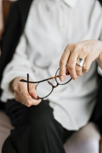 Eine Frau in professioneller Kleidung hält eine Brille in der Hand und wirkt nachdenklich. Die Szene vermittelt eine reflektierte Gesprächsatmosphäre. Solche ruhigen Momente sind typisch in einer ADHS Therapie in der Schweiz.