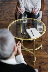 Zwei Personen sitzen sich in einem Therapieraum gegenüber, dazwischen ein Glastisch mit Wasser und Notizbuch. Die Szene steht für einen offenen und vertraulichen Austausch. Solche Gespräche sind zentral für die ADHS Therapie in der Schweiz.