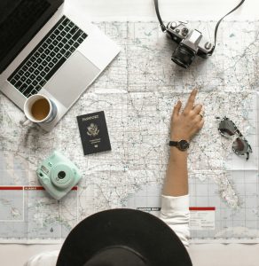Eine Person plant ihre nächste Reise und zeigt auf eine Landkarte, umgeben von Laptop, Kamera, Pass und Kaffee. Für Menschen mit ADHS kann Reiseplanung helfen, Reizüberflutung vorzubeugen – gerade in der Schweiz, wo strukturierte Vorbereitung essenziell sein kann.