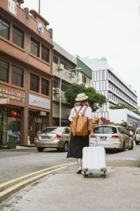 Eine Frau mit Hut und Rucksack zieht einen Koffer durch eine geschäftige Stadtstraße. Menschen mit ADHS erleben in urbaner Umgebung oft Reizüberflutung – insbesondere auf Reisen in der Schweiz, wo neue Eindrücke und Reize schnell überfordern können.