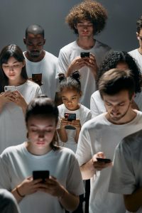 Eine Gruppe von Menschen, darunter auch ein Kind, steht dicht gedrängt in weißer Kleidung und starrt gebannt auf ihre Smartphones. Alle wirken isoliert, obwohl sie beisammen stehen. Das Bild veranschaulicht eindrucksvoll die sozialen Auswirkungen von übermäßiger Bildschirmnutzung – ein zentrales Thema bei ADHS Schweiz.