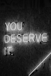 Leuchtende Neonschrift auf einer Holzpaneelwand mit der Botschaft „YOU DESERVE IT“. Die Worte strahlen Motivation und Selbstwert aus. Diese Botschaft stärkt das Selbstbild – ein entscheidender Faktor in der Behandlung von ADHS Schweiz.