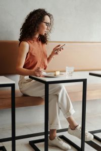 Eine Frau sitzt in einem Café, isst ein Stück Kuchen und schaut gleichzeitig auf ihr Smartphone. Multitasking beim Essen und Smartphone-Nutzung wird oft im Kontext von ADHS Schweiz kritisch betrachtet. Das Bild illustriert die moderne digitale Ablenkung.