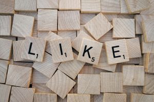 Scrabble-Steine bilden das Wort "LIKE" auf einem Hintergrund aus Holzklötzen. Das Bild symbolisiert die Suche nach Bestätigung in sozialen Medien. Besonders bei ADHS Schweiz wird die Bedeutung von Likes und Online-Interaktionen diskutiert.