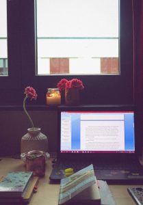 Ein liebevoll gestalteter Lernplatz mit Blumen, Kerze und Laptop vor dem Fenster schafft eine angenehme Atmosphäre. Für Menschen mit ADHS in der Schweiz kann ein solcher Rückzugsort entscheidend sein, um Reizüberflutung zu vermeiden und konzentriert zu arbeiten. Die visuelle Ordnung fördert Ruhe und Fokus.