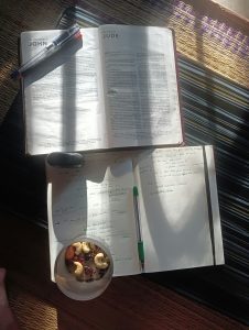 Ein Lernplatz mit Notizen, Bibeltexten und einem gesunden Snack bei Sonnenlicht. Diese ruhige Szene steht im Kontrast zur häufigen Reizüberflutung, die viele Menschen mit ADHS in der Schweiz im Studienalltag erleben. Strukturierte Pausen und bewusste Rituale können helfen, den Fokus zu halten.