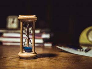 Eine klassische Sanduhr aus Holz steht auf einem Schreibtisch, im Hintergrund sind Bücher und eine Uhr unscharf erkennbar. Die Szene symbolisiert den bewussten Umgang mit Zeit, ein wichtiges Thema bei ADHS Schweiz. Strukturierte Zeitplanung kann Betroffenen helfen, den Alltag besser zu bewältigen.