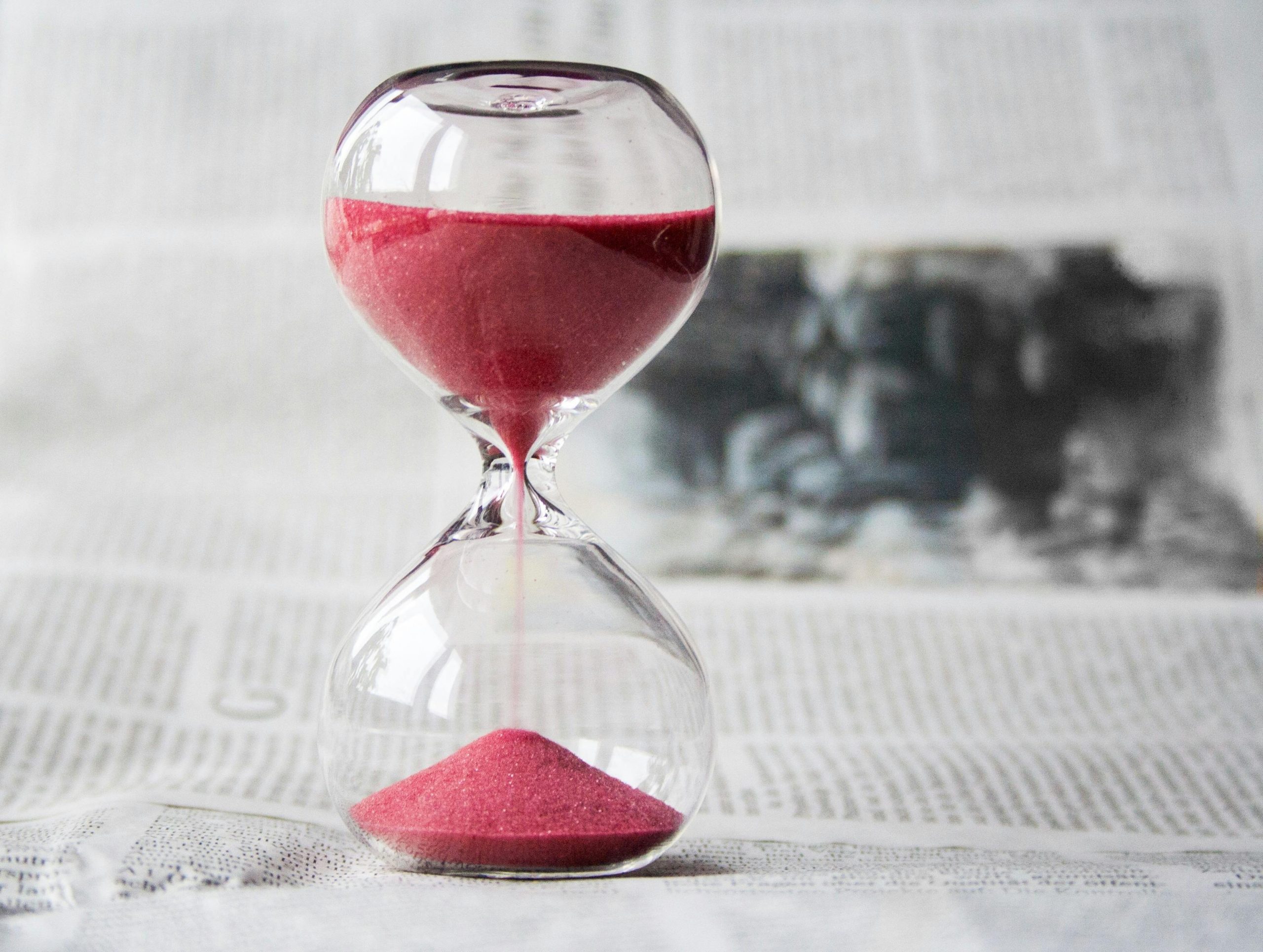 Eine Sanduhr mit rotem Sand läuft auf einer Unterlage aus Zeitungspapier ab. Der Einsatz von visuellen Zeitmessern wird bei ADHS Schweiz als hilfreiche Strategie empfohlen, um Zeitbewusstsein und Aufgabenmanagement zu verbessern. Gerade bei längeren Aufgaben helfen solche Hilfsmittel, die Konzentration aufrechtzuerhalten.