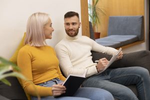 Zwei junge Erwachsene tauschen sich während einer Gruppentherapie oder eines ADHS-Coachings aus – mit Notizbüchern in einer gemütlichen Therapielounge.