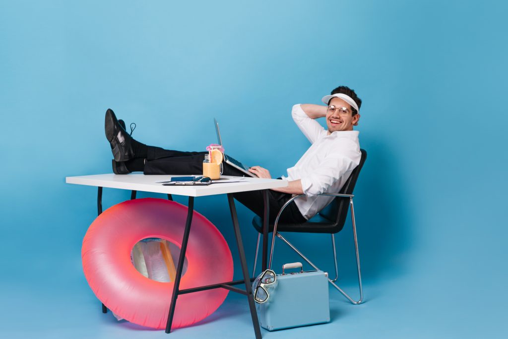 Ein Mann in Businesskleidung sitzt lässig mit Sonnenvisier und Cocktail am Schreibtisch, ein Schwimmring lehnt am Tisch. Work-Life-Balance ist auch bei ADHS Schweiz ein wichtiges Thema, um Überforderung zu vermeiden. Das Bild vermittelt auf humorvolle Weise die Notwendigkeit von Leichtigkeit im Alltag.