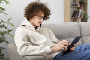 A young man with curly hair sits relaxed on a sofa, using a tablet. In Switzerland, ADHD is increasingly being treated digitally – telemedicine services are making it easier for young people in particular to access psychological support. This digital therapy form adapts to everyday life and promotes low-threshold care.
