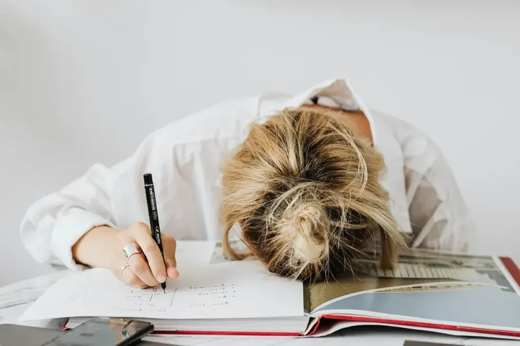 Erschöpfte Frau legt den Kopf auf ihre Unterlagen am Schreibtisch