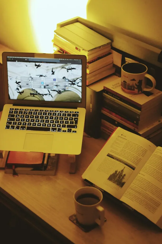 Ein improvisierter Schreibtisch mit Laptop, Büchern und Kaffee symbolisiert intensives Lernen in der Abendstimmung. Gerade in der Schweiz kämpfen viele Studierende mit ADHS gegen die ständige Reizüberflutung an, die durch digitale und analoge Medien entsteht. Ein klarer Arbeitsplatz kann dabei unterstützend wirken.