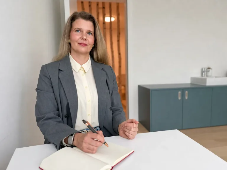 Fachärztin der klaro ADHS Praxis in Zürich sitzt lächelnd am Schreibtisch mit Notizbuch