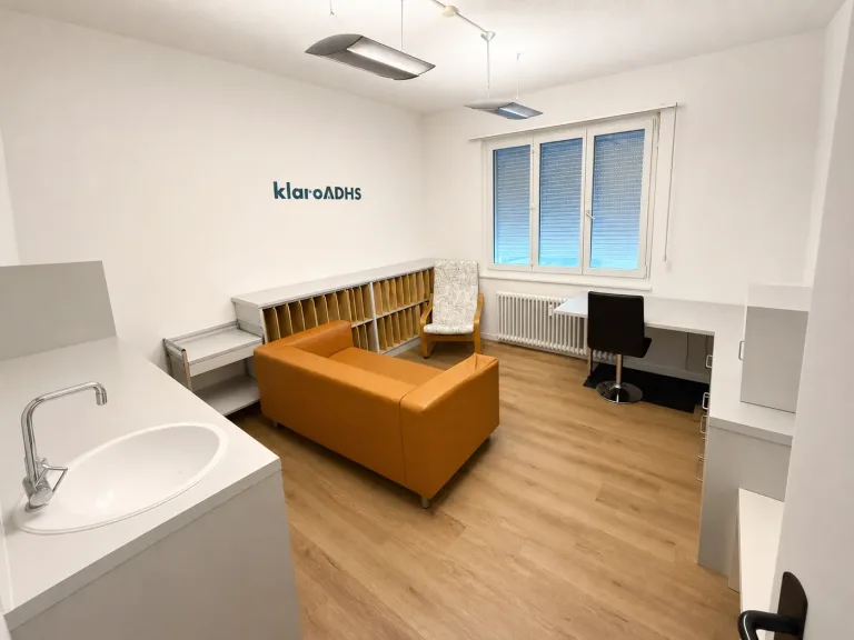 Heller Gesprächsraum der klaro ADHS Praxis in Biel mit Sofa und Logo an der Wand